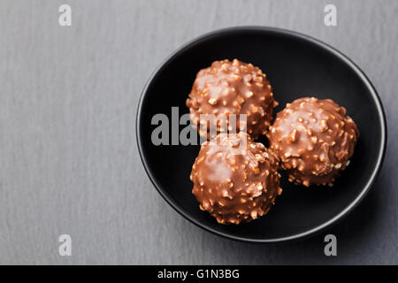 Pralinen, Trüffel in schwarzen Keramikschale auf grauem Schiefer Hintergrund Kopie Raum Draufsicht. Stockfoto