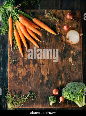 Hölzerne gesunde Ernährung Hintergrund mit rohem Gemüse und Kräutern. Brokkoli, Karotten, Zwiebeln und Thymian über hölzerne strukturierte Oberfläche. Stockfoto