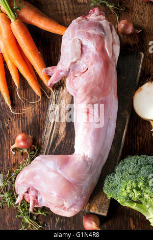Rohe ungekochte ganze Kaninchen mit frischem Gemüse und Kräutern auf Holz hacken an Bord über alte Holz Hintergrund. Ansicht von oben Stockfoto
