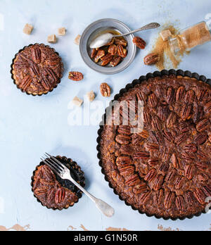 Hausgemachte große Runde Karamell Pecan Pie und kleine Törtchen in schwarzem Eisen Formen, serviert mit braunem Zucker, Karamell-Sauce und vintage Stockfoto