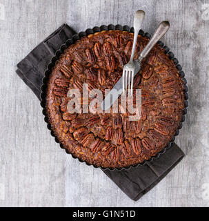 Hausgemachte große Runde Karamell Pecan Pie in schwarzem Eisen Formen, serviert mit Vintage Besteck auf schwarzem Textil Serviette über grau strukturiert Stockfoto