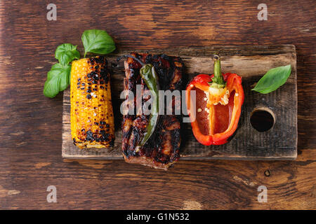 Grill gegrillte Schweinerippchen, Mais, grünem Chili und Paprika serviert auf Schneidbrett aus Holz mit frischem Basilikum über hölzerne backg Stockfoto