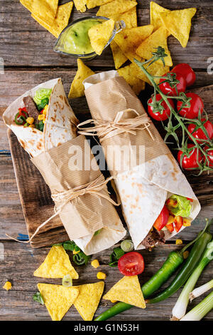 Abendessen im mexikanischen Stil. Zwei tapezierte Tortillas Burrito mit Rindfleisch und Gemüse serviert mit Gemüse, Nachos Chips und guacomole Stockfoto