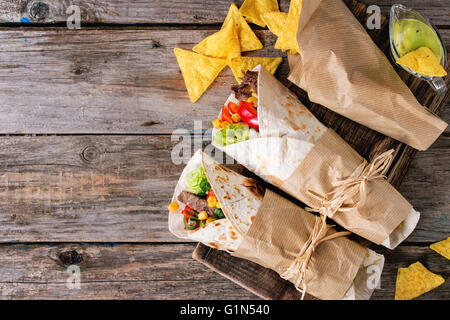 Abendessen im mexikanischen Stil. Zwei tapezierte Tortillas Burrito mit Rindfleisch und Gemüse serviert mit Nachos Chips und Guacomole Soße über o Stockfoto