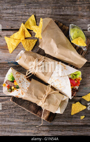 Abendessen im mexikanischen Stil. Zwei tapezierte Tortillas mit Rindfleisch und Gemüse serviert mit Nachos Chips und Guacomole Soße über alte woode Stockfoto