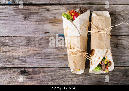 Abendessen im mexikanischen Stil. Zwei Tortillas mit Rindfleisch und Gemüse über alten hölzernen Hintergrund tapeziert. Flach zu legen. Mit Textfreiraum Stockfoto