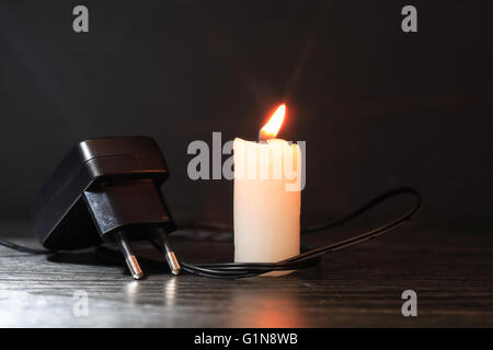 Blackout-Konzept. Elektro-Ladegerät mit Kabel in der Nähe von Beleuchtung Kerze auf dunklem Hintergrund Stockfoto