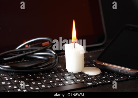 Blackout-Konzept. Kerze anzünden auf Laptop in der Nähe von Kabel Stockfoto