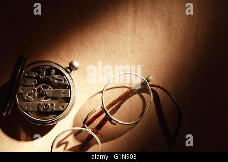 Alte Brille in der Nähe von geschlossenen Taschenuhr auf braunem Papierhintergrund Stockfoto