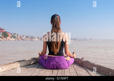 Junge Frau praktizieren Yoga-Meditation auf dem Boot über den Fluss Ganges, Indien Stockfoto