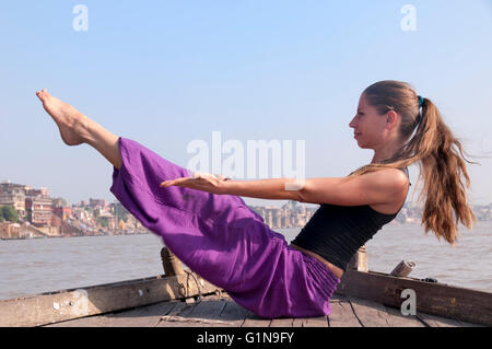 Junge weibliche Praktizierende Yoga pose Navasana auf dem Boot über den Fluss Ganges, Indien Stockfoto