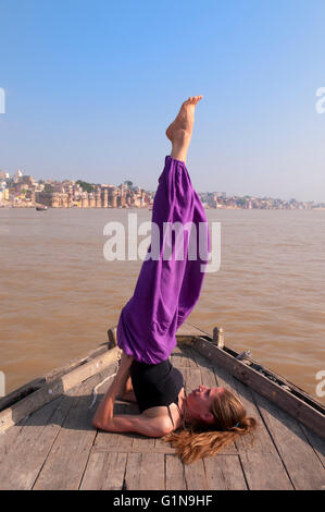 Junge weibliche Praktizierende Yoga pose Sarvangasana auf dem Boot über den Fluss Ganges, Indien Stockfoto