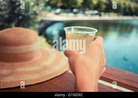 Eine junge Frau ist von einem Teich im Park Limonade trinken. Stockfoto