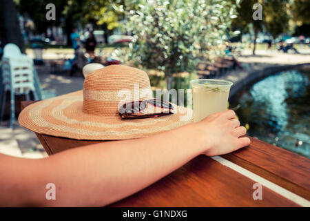 Eine junge Frau ist von einem Teich im Park Limonade trinken. Stockfoto