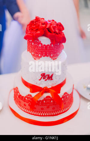 Weiße Hochzeitstorte dekoriert mit frisch vermählte Anfangsbuchstaben, Bändern und rote Blüten an der Spitze Stockfoto