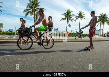 RIO DE JANEIRO - 6. März 2016: Brasilianer auf dem Fahrrad schleppen einen Freund auf einem Skateboard unterwegs am Strand vor Ipanema Stockfoto