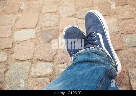 Entspannende männliche Füße in blauem Segeltuch-Sportschuh auf alten grobe Steinpflaster Stockfoto