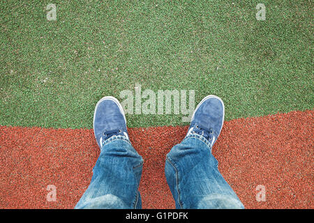 Männliche Füße in Blue Jeans und Turnschuhe stehen auf künstliche Stadion Rasen Stockfoto