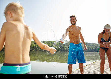 Vater und Sohn besprühen einander mit Wasser an einem See im Sommer Stockfoto