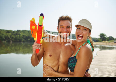 Glückliches Paar an einem See mit Spritzpistolen, Spaß haben und lachen Stockfoto