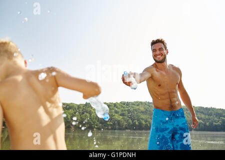 Glücklicher Vater und Sohn besprühen einander mit Wasser an einem See im Sommer Stockfoto