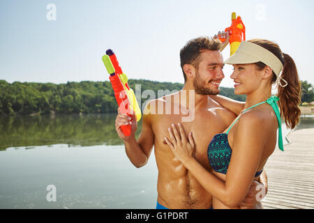 Glückliches Paar in Liebe an einem See mit Spritzpistolen umarmen einander Stockfoto