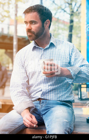gut aussehender Mann draußen zu sitzen und trinken aus einer Tasse Stockfoto