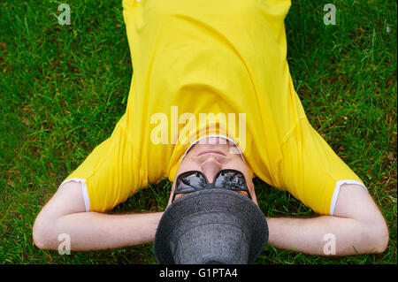 Mann in einem gelben T-shirt und Hut auf dem Rasen liegend Stockfoto