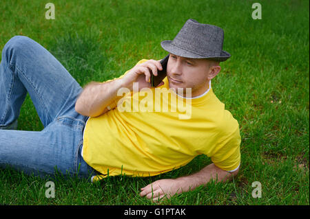 kluger junger Mann in ein gelbes T-shirt mit dem Telefon auf dem Rasen Stockfoto