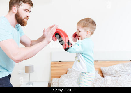 Niedlichen kleinen Sohn in Boxhandschuhe mit seinem Vater zu Hause spielen