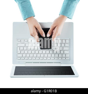 Frau, die über einen Touchscreen smart Telefon und einen Laptop auf weißem Hintergrund, Hände hautnah, Ansicht von oben Stockfoto