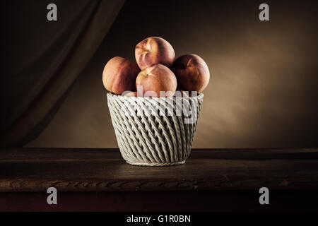 Reife Pfirsiche in einem weißen Korb auf einem rustikalen Holztisch und drapieren auf Hintergrund, Obst-Stilleben Stockfoto