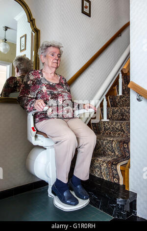 Ältere Frau mit Treppenlift / Treppe Segelflugzeug, mechanische Vorrichtung zum Heben von Personen zu Hause die Treppen hoch und runter Stockfoto