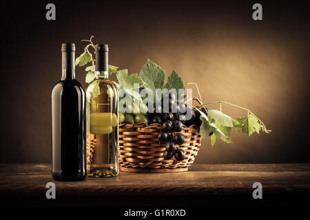 Flaschen Wein, Trauben und Weinblättern in einem Korb auf einem rustikalen Holztisch, Stilleben Stockfoto