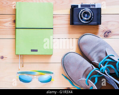 Satz von Reise- und Resort Zeug. Alten 35 mm-Kamera, Notizbuch, Sonnenbrillen und Desert-Boots auf Holztisch. Ansicht von oben flach legen Stockfoto