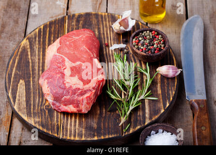 Rohes Frischfleisch Steak mit Salz und Pfeffer, Rosmarin und Tomaten auf Schneidebrett auf dunklem Holz. Textfreiraum Stockfoto