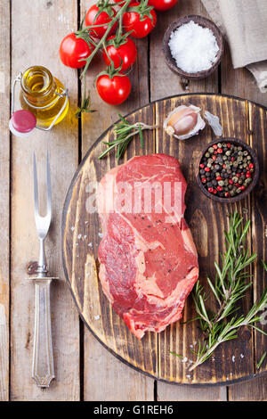 Rohes Frischfleisch Steak mit Salz und Pfeffer, Rosmarin und Tomaten auf Schneidebrett aus Holz dunkel Draufsicht Stockfoto