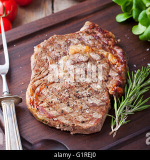 Rindersteak mit Cherry Tomaten und Rosmarin auf einem dunklen Schneidebrett aus Holz Hintergrund. Stockfoto