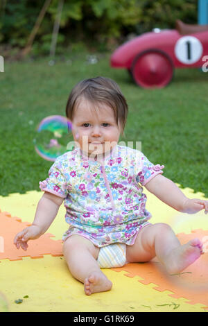 Babymädchen setzte sich gerade Blase schweben durch im Garten Stockfoto