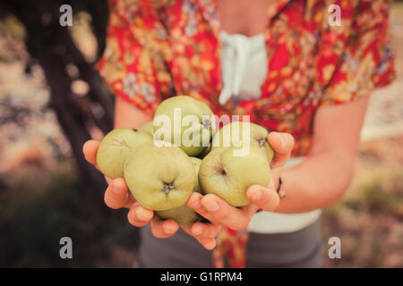 Eine junge Frau steht unter einem Baum und hält ein paar Äpfel Stockfoto