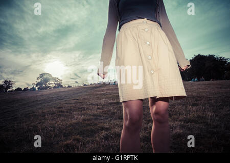 Eine junge Frau den Rock weht im Wind, wie sie bei Sonnenuntergang in einem Park steht Stockfoto