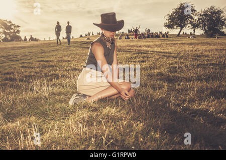 Eine junge Frau sitzt auf einem Hügel im Park bei Sonnenuntergang Stockfoto