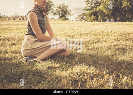 Eine junge Frau sitzt auf einem Hügel im Park bei Sonnenuntergang Stockfoto