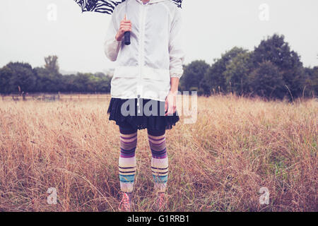 Eine junge Frau mit einem Regenschirm steht in einem Feld Stockfoto