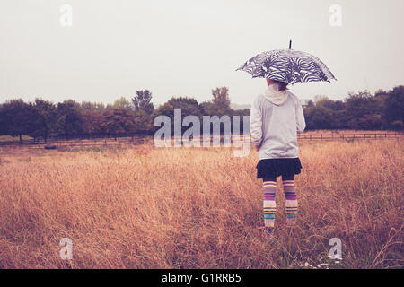 Eine junge Frau mit einem Regenschirm steht in einem Feld Stockfoto