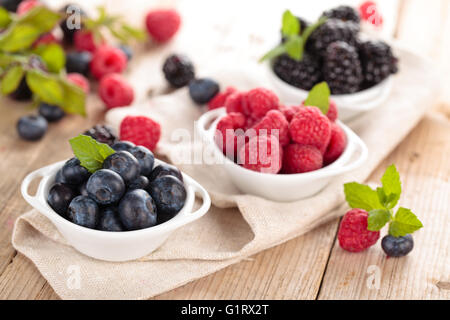 Heidelbeeren, Brombeeren und Himbeeren in kleinen weißen Schalen. Mit Minze. Auf Holztisch. Stockfoto