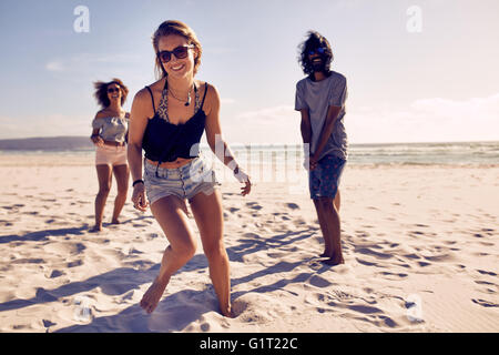 Porträt der schönen jungen Frau am Strand mit Freunden im Hintergrund genießen. Heterogene Gruppe von Freunden genießen Strand holi Stockfoto
