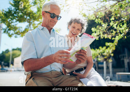 Älteres Ehepaar sitzt im Freien in der Stadt, Blick auf eine Karte. Senior glücklich mit seiner Frau mit Stadtplan. Stockfoto