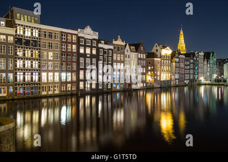 Alte Gebäude entlang der Damrak in Amsterdam bei Nacht. Reflexionen im Wasser zu sehen. Stockfoto