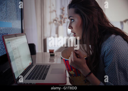 Schockiert gefragt, junge Frau mit Laptop und Essen Popcorn zu Hause Stockfoto